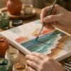 Hands painting numbered canvas close up Two hands applying teal paint to a numbered seascape section with paint pots